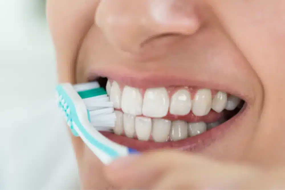 Close-up of a person brushing their teeth with a toothbrush, showing clean white teeth and healthy gums.